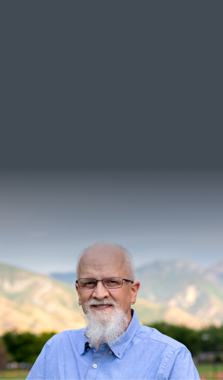 Dan, male patient with PBA in his 60s, standing in front of a mountainous landscape