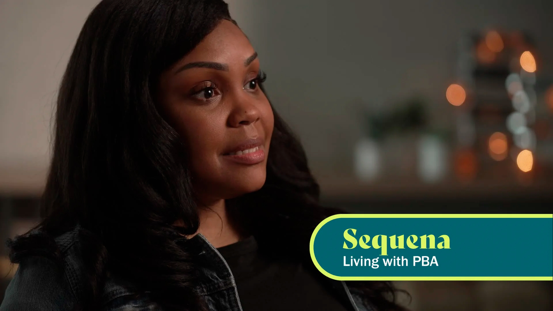 An African American woman with long brown hair is seen in profile, facing to the right. The caption on screen says “Sequena, living with PBA.”