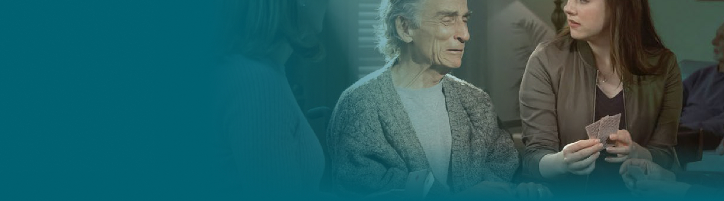 Actor portrayals of an older male experiencing Pseudobulbar Affect (PBA) crying symptoms, next to a younger female holding playing cards